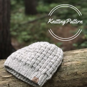 May include: A light gray knitted beanie with a woven pattern, resting on a wooden log. The hat features a folded brim and a small tag. The words "Knitting Pattern" are in white script above the hat.