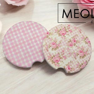 May include: Two pink and white patterned coasters. One coaster has a pink and white gingham pattern. The other coaster has a floral pattern with pink roses on a white background. The coasters are made by Meola & Company.