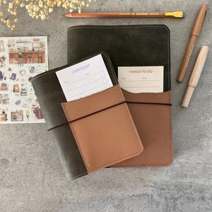 May include: A leather journal with a brown cover and a pocket holding a checklist. A second journal with a brown pocket holds a "Things to Do" card. A pencil and two pens are also visible.