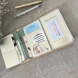 Puede incluir: Un organizador de agenda de tres pliegues con exterior y bolsillos interiores de color crema. Contiene una tarjeta azul 'THIS WEEK'S SCHEDULE', una lista 'TO DO' y una tarjeta blanca con la palabra 'PLANNING' impresa verticalmente.