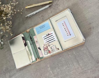 May include: A tri-fold planner organizer with a cream-colored exterior and interior pockets. It contains a blue 'THIS WEEK'S SCHEDULE' card, a 'TO DO' list, and a white card with the word 'PLANNING' printed vertically next to a pink pencil graphic.