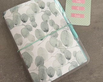 May include: A notebook with a clear plastic cover, decorated with a eucalyptus leaf design. A light blue pen and a card with the text "lots of love" are included. The card has a light green background with white heart shapes.