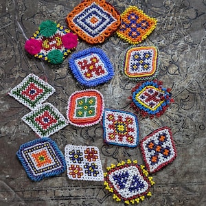 May include: A collection of colorful, beaded decorative patches in various geometric shapes. The patches feature intricate patterns in red, blue, orange, yellow, and green beads. Some patches have a diamond or square shape, while others have a more rounded form.