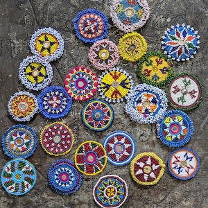 May include: A collection of colorful, beaded circular ornaments. The ornaments feature intricate patterns in various colors, including blue, yellow, red, and white. Some have mirrored centers. The beads are arranged in concentric circles and starburst designs.