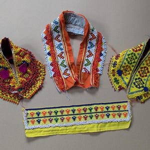May include: A collection of four textile accessories featuring intricate beadwork. Three pieces are collar-like shapes in orange, yellow, and red with geometric patterns, while the fourth is a rectangular yellow band with colorful beaded motifs.