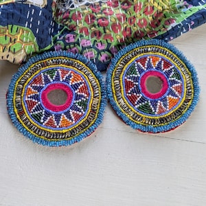 May include: Two circular embroidered patches featuring intricate beadwork in vibrant shades of blue, orange, green, and white. Each patch has a central circular mirror surrounded by a bright pink border, with concentric rings of beads and metallic accents.