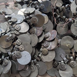 Puede incluir: Un montón de colgantes antiguos de metal plateado. Cada colgante tiene un disco circular con un elemento decorativo y un lazo para colgar. Los colgantes están deslustrados, mostrando signos de edad y desgaste.