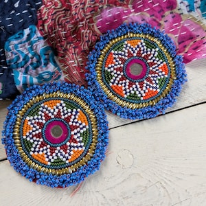 May include: Two circular patches featuring intricate beadwork in blue, orange, white, green, and red. Each patch has a central circular mirror surrounded by concentric rings of beads, including metallic gold accents and a vibrant blue beaded border.