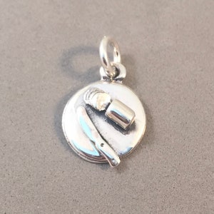 May include: A silver charm featuring a plate with a knife, a roll of sliced food, and a small container. The charm has a loop at the top for attaching to a necklace or bracelet. The charm is made of shiny metal.