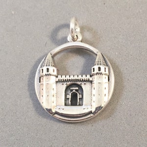 May include: A silver-colored pendant featuring a detailed castle design within a circular frame. The castle has two towers, a central gate, and a crenelated wall. The pendant includes a small loop for attaching to a chain or bracelet.