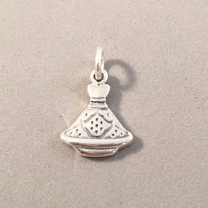 May include: A small, silver-colored charm in the shape of a dress. The charm has a detailed design on the skirt portion, with small circular cutouts. The dress charm has a loop at the top for attaching to a necklace or bracelet. The charm is on a gray background.