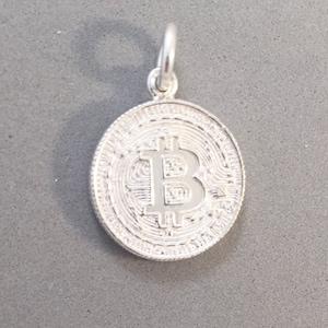 Può includere: Un ciondolo Bitcoin color argento con un anello per una catena. Il ciondolo presenta il simbolo Bitcoin al centro, circondato da un bordo strutturato e dettagliato. Il ciondolo a forma di moneta è progettato per assomigliare a un Bitcoin fisico.