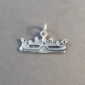 Peut inclure: Un petit charm en argent en forme de bateau. Le charm présente des détails complexes sur la coque et la structure supérieure, avec une boucle en haut pour l'attache. Le charm de bateau est probablement destiné à un collier ou un bracelet.