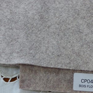 Puede incluir: Dos muestras de tela de fieltro. La muestra superior es de color gris claro. La muestra inferior es de color marrón claro. Una etiqueta blanca con texto negro dice "CP048 BOIS FLOTTE".