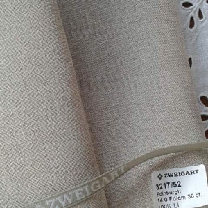 Op de afbeelding: Twee stukken beige linnen stof met een wit label met de tekst "ZWEIGART 3217/52 Edinburgh 14,0 Fd/cm 36 ct. 100% LI"