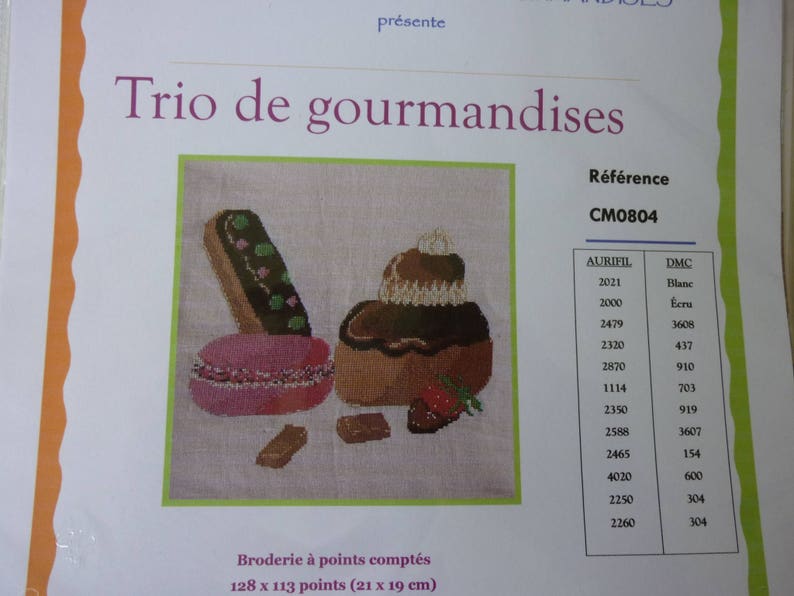 May include: A cross-stitch pattern for a trio of pastries, including a chocolate eclair, a cake with strawberries, and a macaron. The pattern includes a color chart with DMC and Aurifil thread numbers.