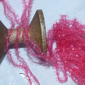 Peut inclure: Une bobine en bois de fil rose pailleté avec une texture duveteuse.