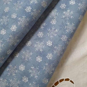 Peut inclure: Tissu bleu avec un motif de flocons de neige blancs. Le tissu est plié en deux, montrant le motif des deux côtés.