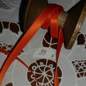 May include: Orange satin ribbon wound around a wooden spool. The spool has a label with the number "39 6" written on it.