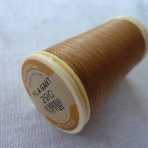 Peut inclure: Une bobine de fil brun avec une étiquette blanche qui indique "Fil A Gant 280".