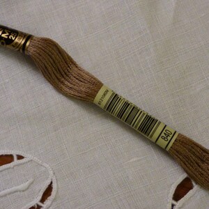 Op de afbeelding: Een bruine DMC borduurgaren met een wit label waarop "DMC Cotton Embroidery Floss" en "840" staat.