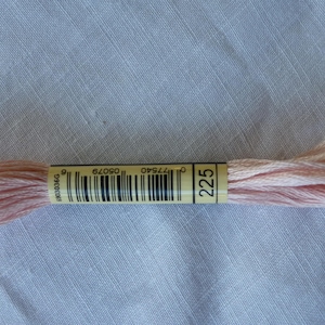 Op de afbeelding: Een spoel roze borduurgaren met een label waarop "225" en een barcode staan. Het label is geel en de tekst is zwart.