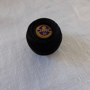 May include: A black ball of DMC embroidery floss with a gold and purple label that reads "DMC 80".
