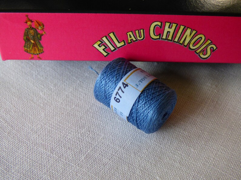 Puede incluir: Una bobina de hilo de bordar azul con el n&uacute;mero 6774 impreso en la etiqueta. La etiqueta tambi&eacute;n dice "Fil au Chinois" y "J. Touche".