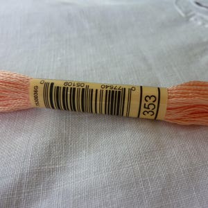 Op de afbeelding: Een spoel met perzikkleurige borduurgaren met een label met de tekst "353", "05106" en "77540".