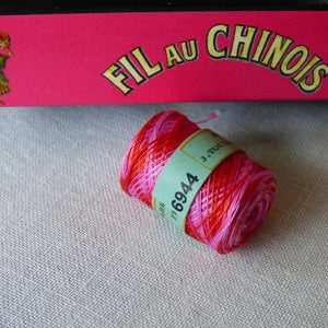 May include: A spool of pink, red and white embroidery floss with a label that reads "Fil Au Chinois" and "6944".