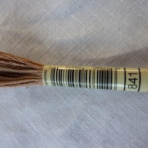 Könnte beinhalten: Eine braune Stickgarnrolle mit einem weißen Etikett, auf dem "841" steht und ein Barcode ist.
