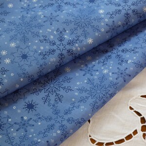 Peut inclure: Tissu bleu avec un motif de flocons de neige blancs. Le tissu est plié en deux et le bord inférieur est visible.