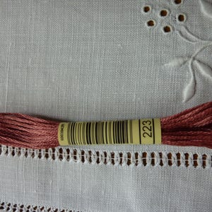 Op de afbeelding: Een klosje borduurgaren in een diepe roze kleur, gelabeld met het nummer "223" en een barcode.