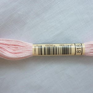 Op de afbeelding: Een roze borduurgaren met een wit label waarop "818" staat en een barcode. Het label heeft ook het nummer "0177540 05253 723000325".