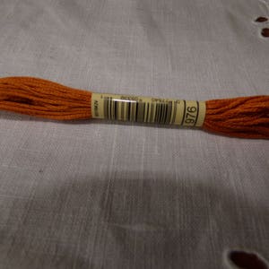 Op de afbeelding: Een spoel oranje borduurgaren met een label met de tekst "DMC 976".
