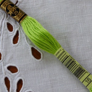 Op de afbeelding: Een klosje DMC borduurgaren in een heldere groene kleur. Het garen is gewikkeld om een kartonnen spoel met een gouden label waarop staat "DMC Special 25m (87 yds) 16 6383005 1X E 077540 62822 00222".
