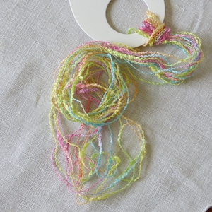 Peut inclure: Une pelote de fil multicolore dans des tons de rose, vert et bleu. Le fil est enroulé autour d'une bobine en plastique blanche.