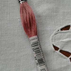 May include: A spool of DMC embroidery floss in color 223, a dusty rose pink. The spool has a white label with black text and a barcode.