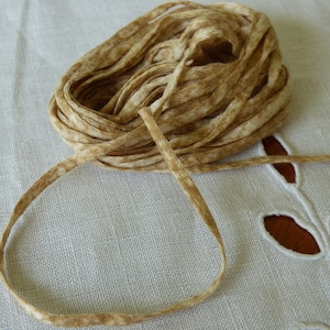 May include: A spool of brown and beige ribbon with a speckled pattern. The ribbon is coiled and tied in a knot.