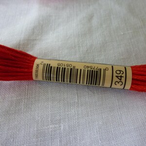 Op de afbeelding: Een spoel rode borduurgaren met een bruin label waarop "349" staat en een barcode. Het barcode-nummer is "0 77540 05105 2".