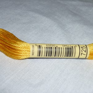 Op de afbeelding: Een spoel gele borduurgaren met een label waarop "725" en een barcode staan. Het label bevat ook de nummers "90270330" en "017540 05203".