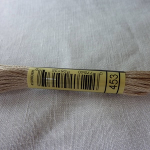 Op de afbeelding: Een klosje lichtbruin borduurgaren met een geel label waarop "453" staat en een barcode. Het label heeft ook de tekst "09135" en "77540".