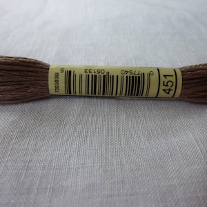 May include: A brown embroidery floss spool with the number 451 printed on a yellow label. The label also includes the numbers 72030361, 077540, and 105733.