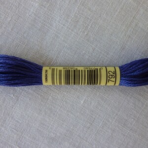 Op de afbeelding: Een klosje DMC borduurgaren in kleur 792, een diepe blauwe tint. Het garen is gewikkeld om een geel label met het DMC-logo en het kleurnummer.