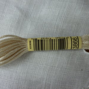 Op de afbeelding: Een spoel met crèmekleurige borduurgaren met een geel etiket waarop "3866" staat en een barcode. Het etiket heeft ook de tekst "077540 74764 633330361".
