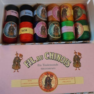 May include: A box of 10 spools of embroidery thread, labeled "Fil au Chinois" with the brand name "Ets Toulemonde" and "Fabrique en France". The spools are in various colors, including black, red, orange, green, and brown.