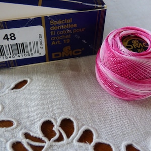 Puede incluir: Una madeja de hilo de crochet DMC rosa y blanco con el número 48 impreso en la etiqueta. La etiqueta también dice "Spécial dentelles fil coton pour crochet Art. 19 DMC".