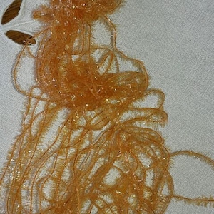 Peut inclure: Une bobine de lamé orange et or scintillant avec une étiquette blanche attachée.