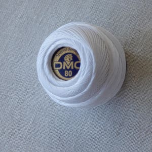 May include: A white ball of DMC embroidery floss with a blue and gold label that says "Special dental DMC 80".