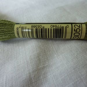 Op de afbeelding: Een groene borduurgaren met een wit label waarop "3052" en een barcode staan. Het label bevat ook de nummers "077540" en "03996".